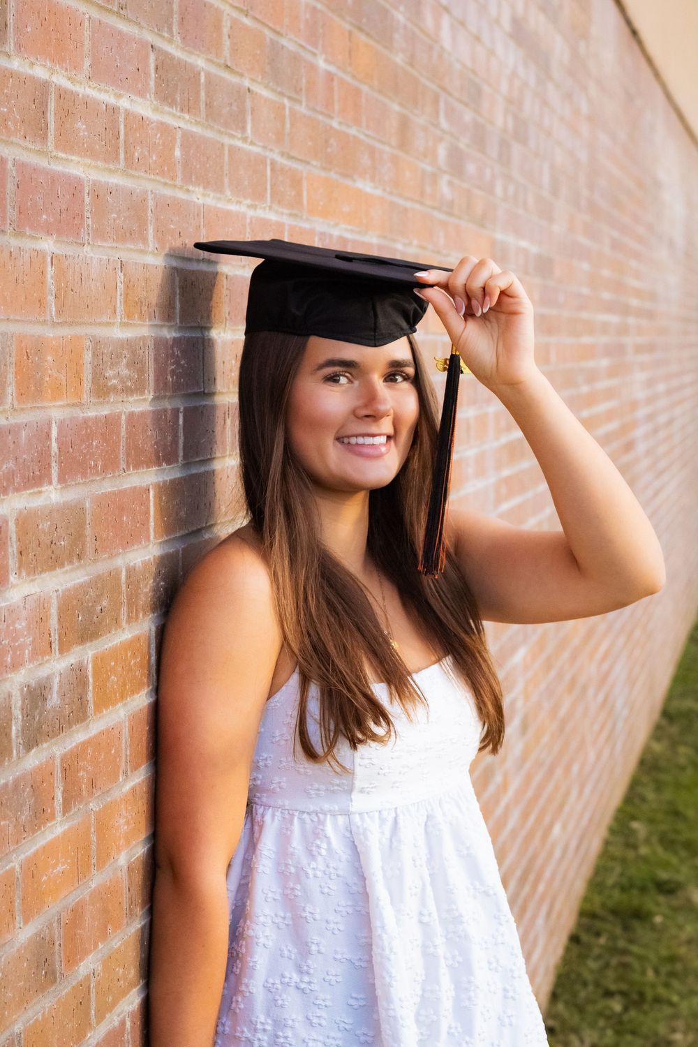 Graduate in white dress poses with cap against brick wall in progression shots.