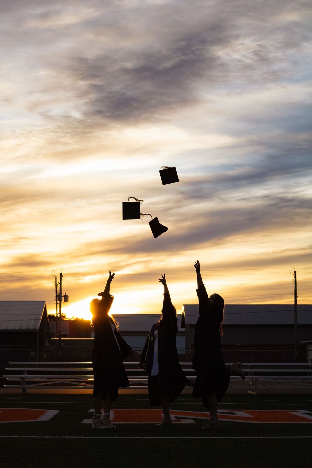 Silhouettes of graduates throwing caps in the air during sunset celebration.