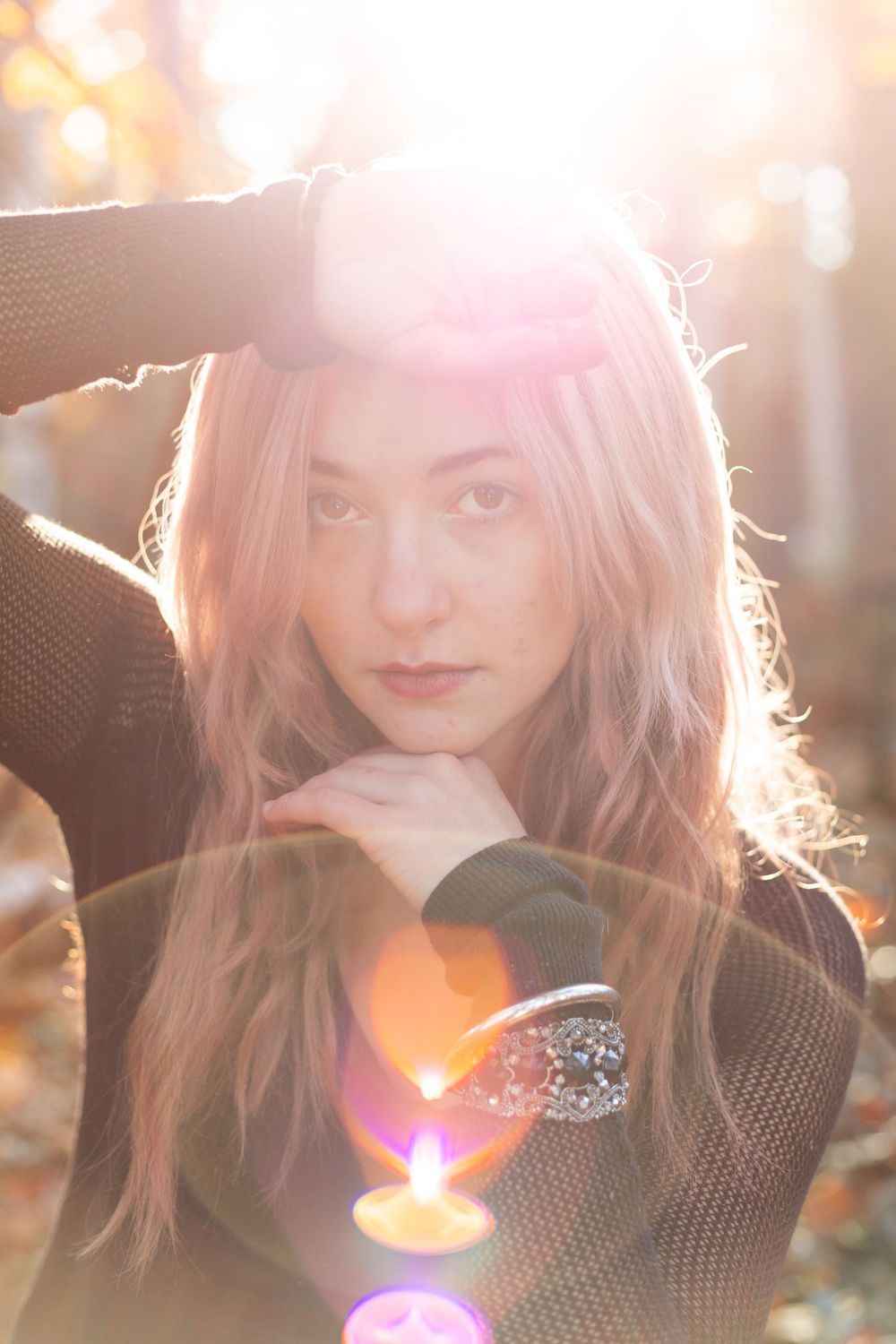 A woman with pink hair poses outdoors in a black sweater as golden sunlight creates a dreamy backlit effect.
