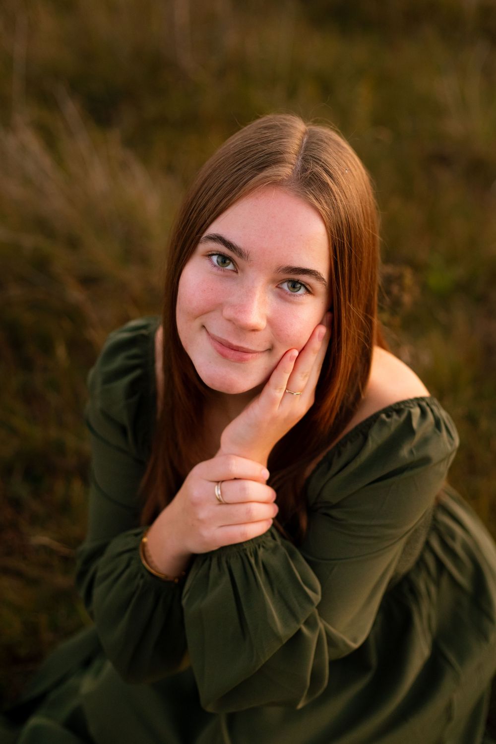 Portrait of person in green dress resting head on hand outdoors at sunset.