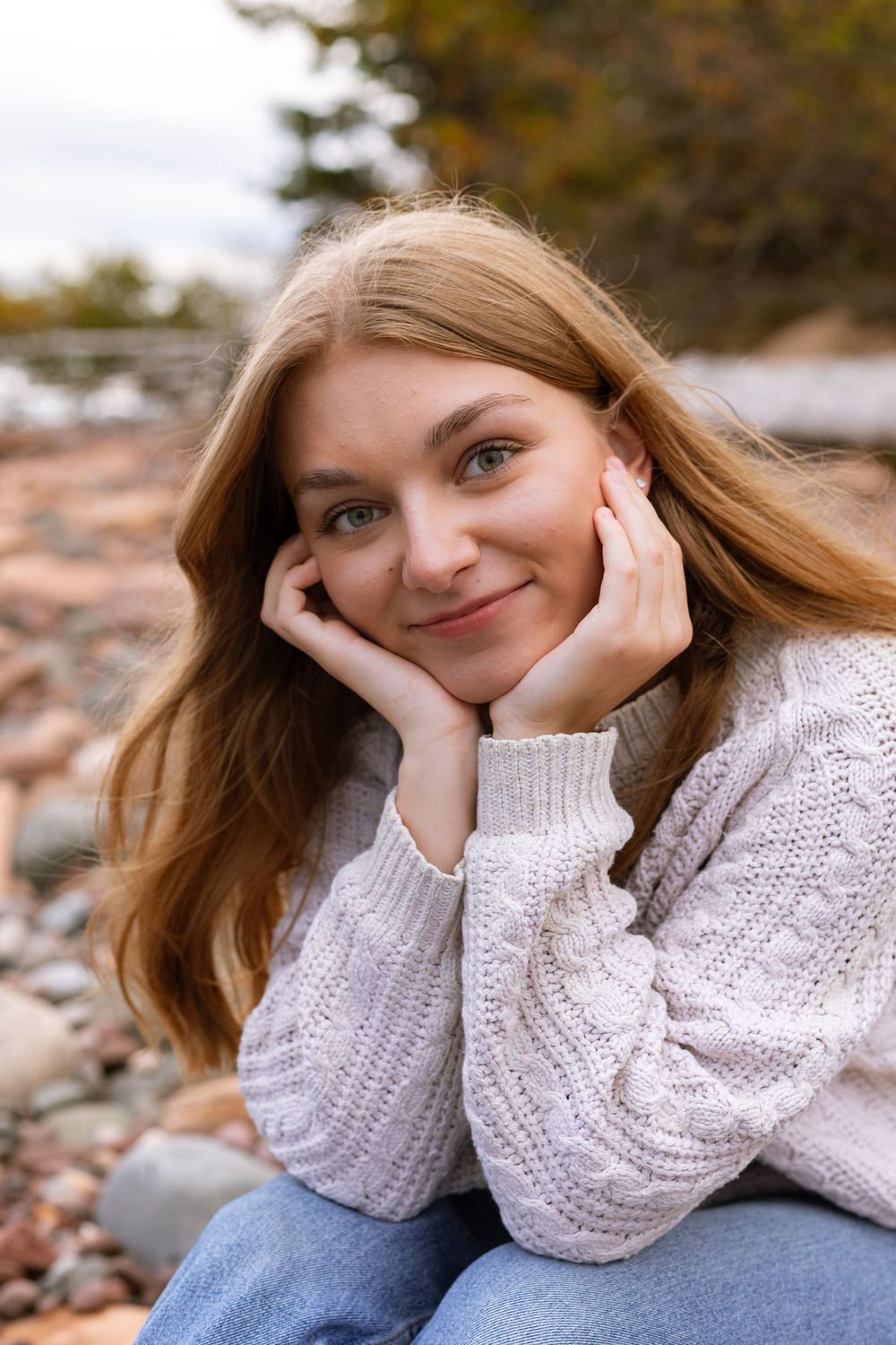 Person in white knit sweater lying on autumn ground with relaxed expression.