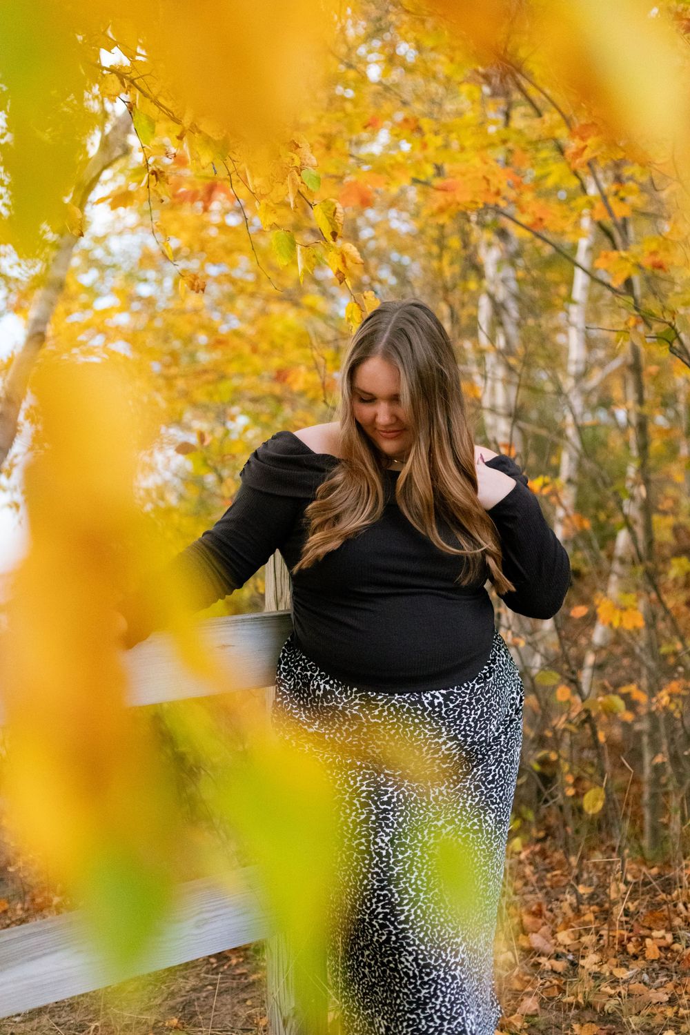 A figure in a black and white polka dot dress poses in front of autumn foliage with golden bokeh effects in the background.