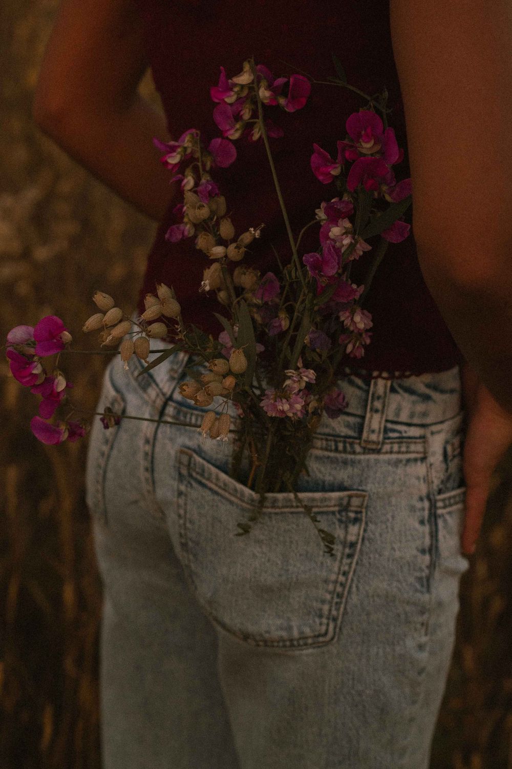 Wildflowers tucked into the back pocket of light wash jeans worn by a person in a dark red top outdoors.