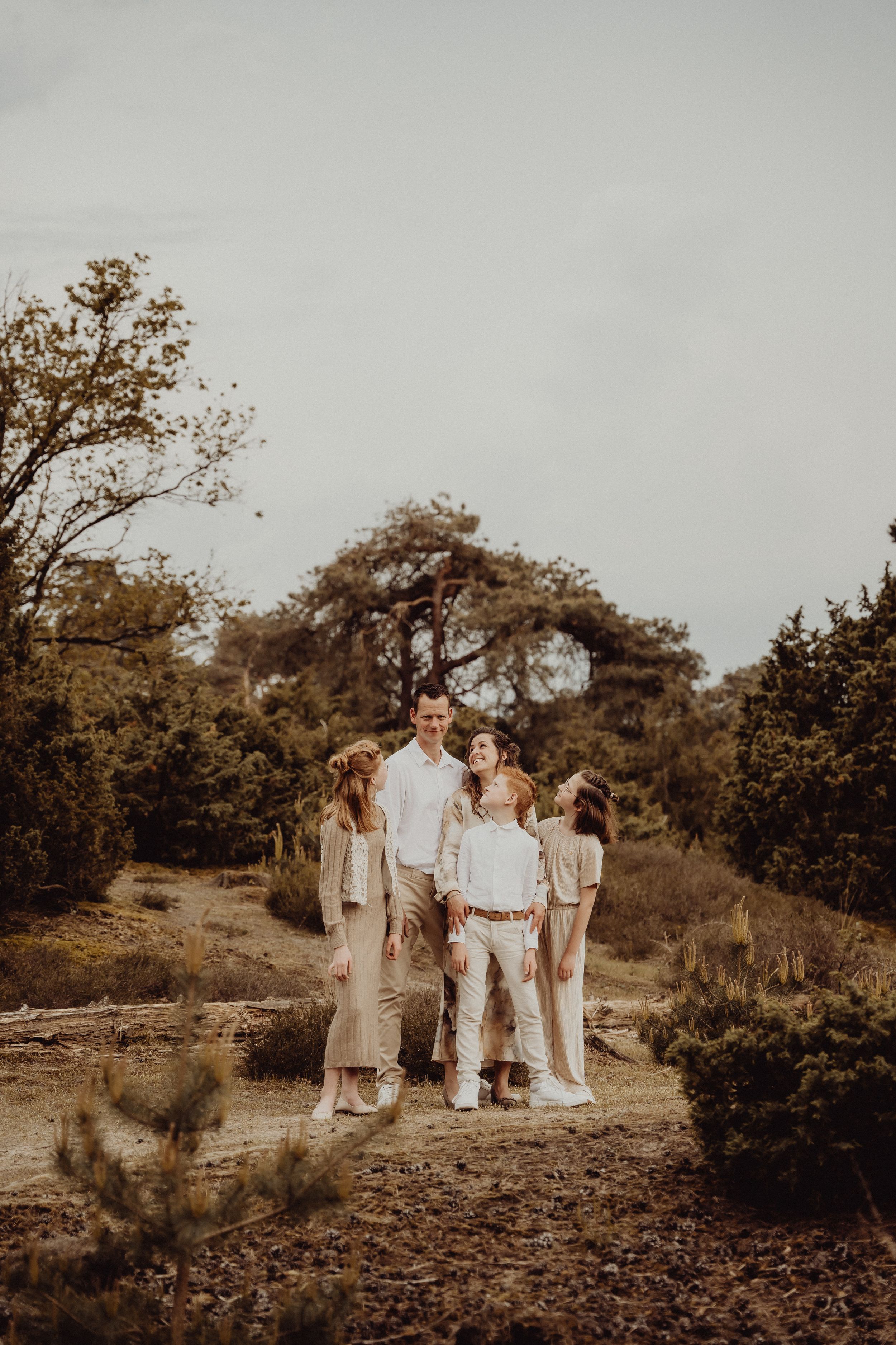 A family portrait in neutral tones photographed outdoors against an autumn landscape.