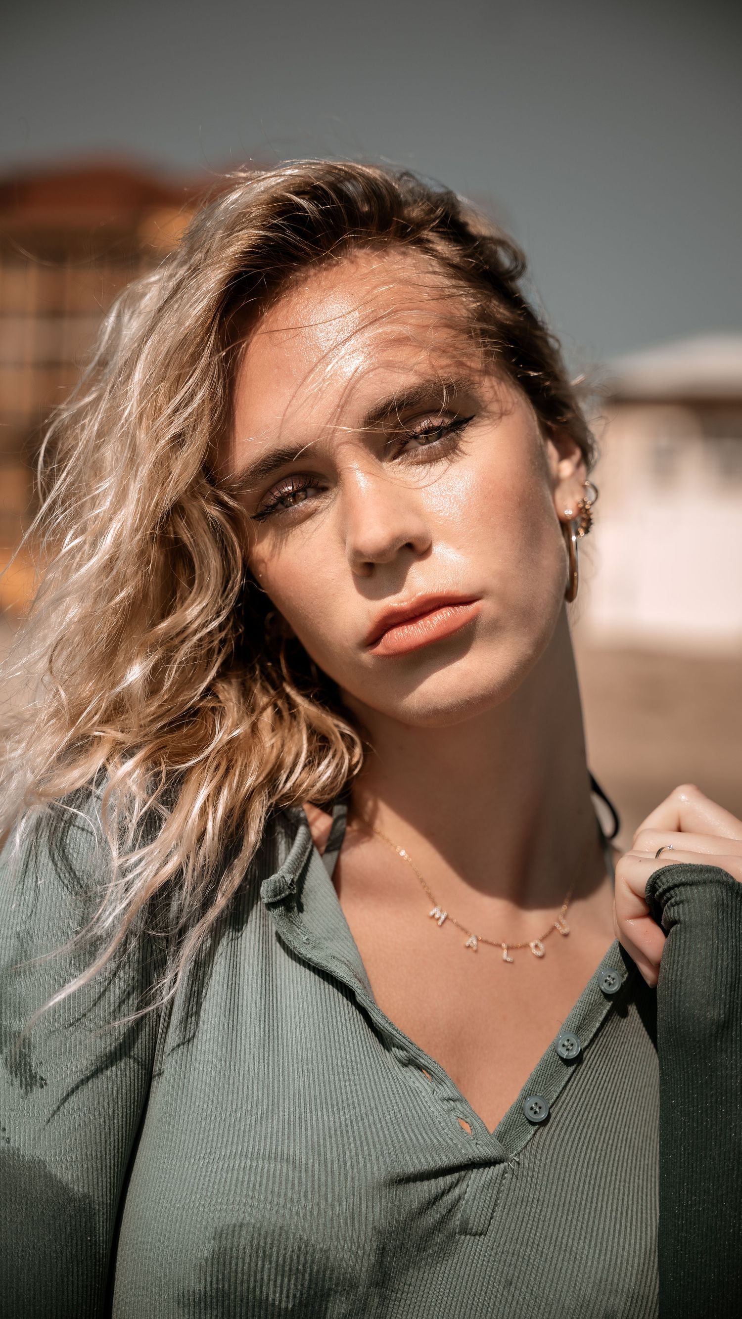 Portrait of model in green top with blonde wavy hair and delicate necklace.