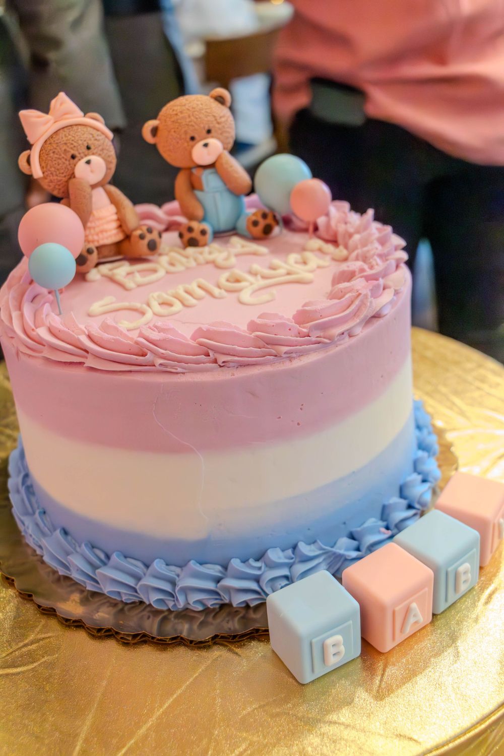 Pink and blue decorated cake with teddy bear toppers and baby blocks for a gender reveal party.
