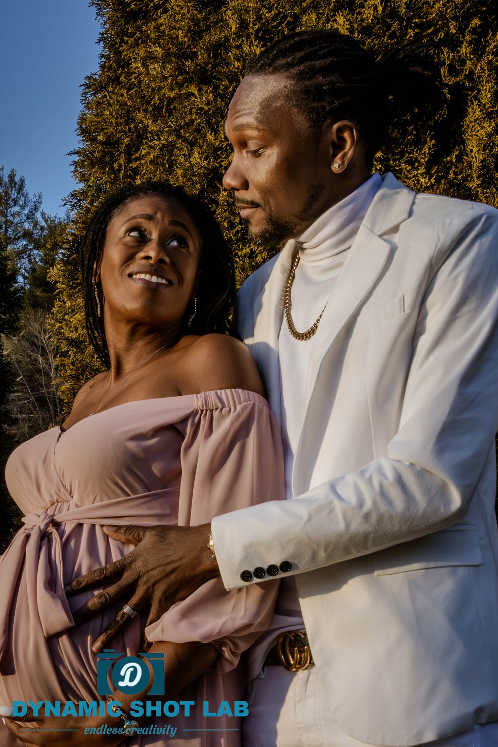 Maternity photoshoot outdoors featuring a pink dress and white suit.