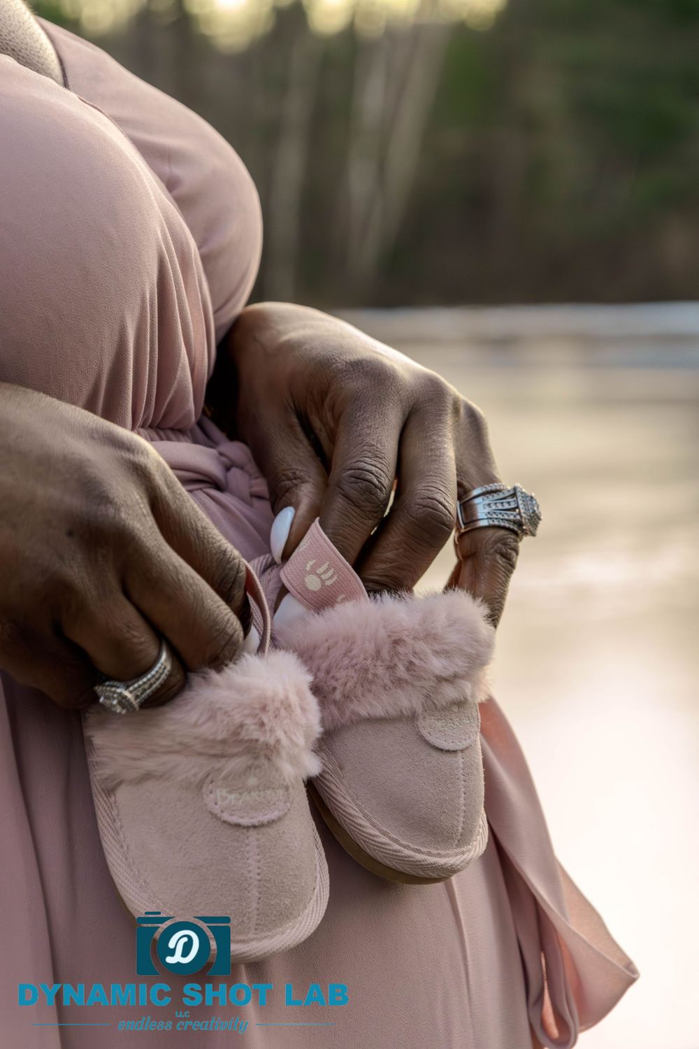 Close-up of hands holding soft pink baby shoes against a blurred natural background.
