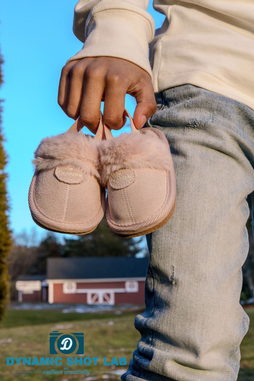 Hand holding small pink baby slippers against a blue sky background.