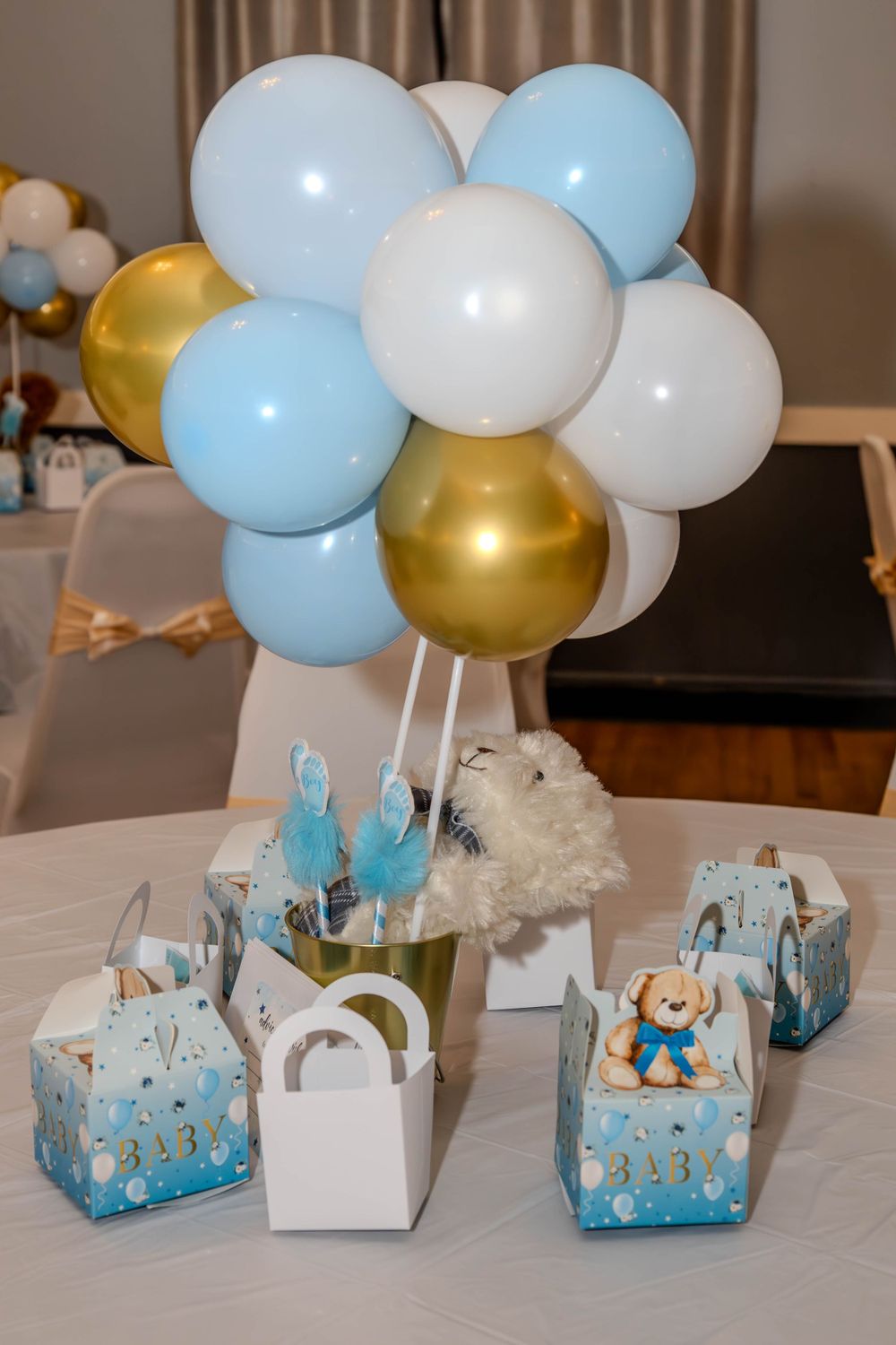 Baby shower decorations with blue and gold balloons alongside gift boxes on a white table.