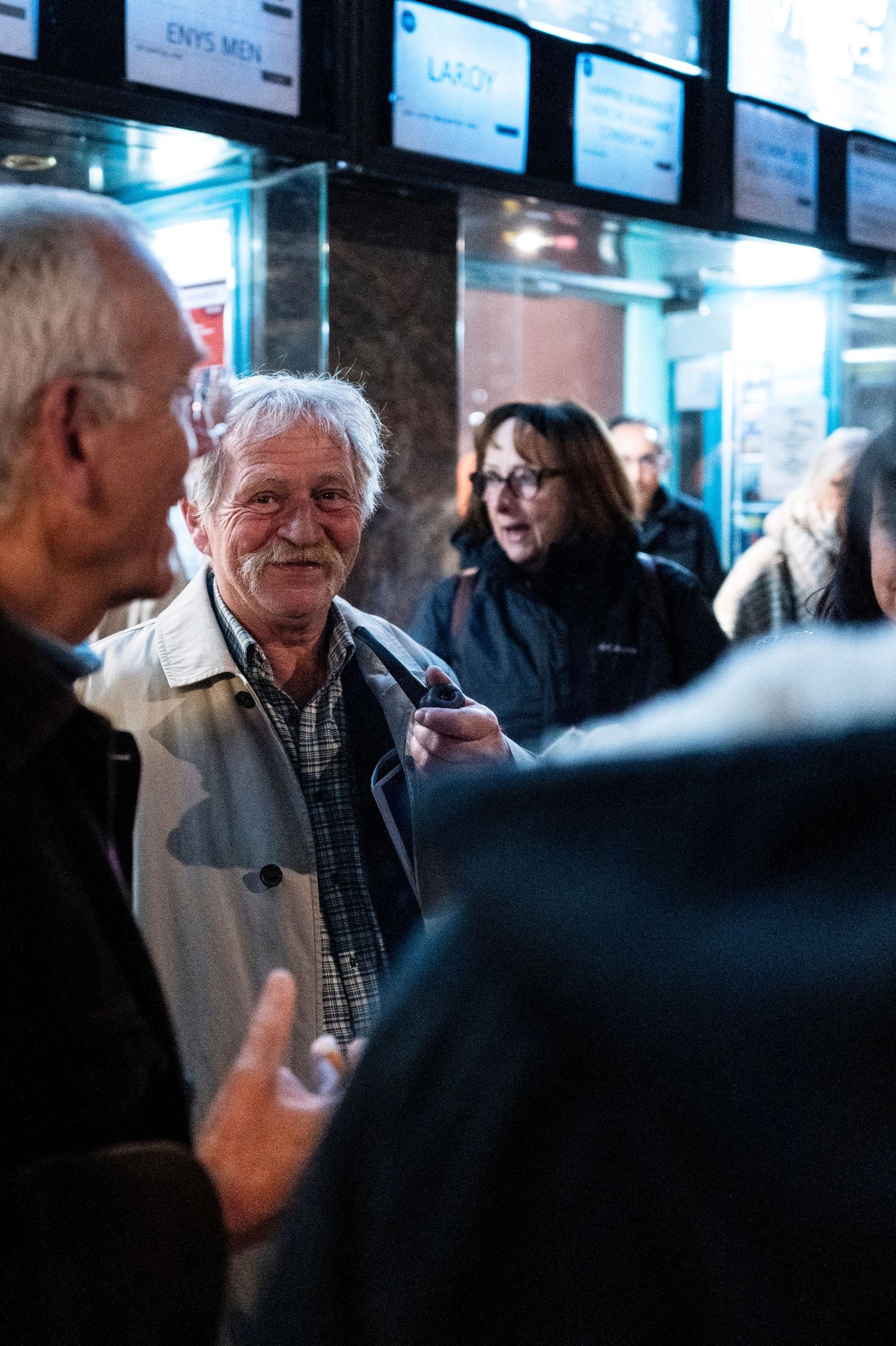 People having animated conversation near illuminated display screens.