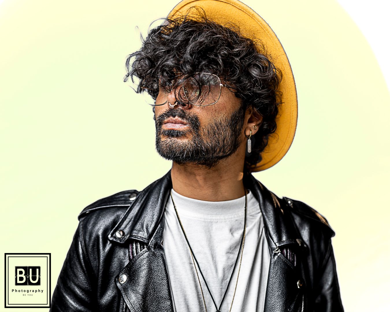 Artistic portrait against yellow backdrop featuring leather jacket and brown hat styling.