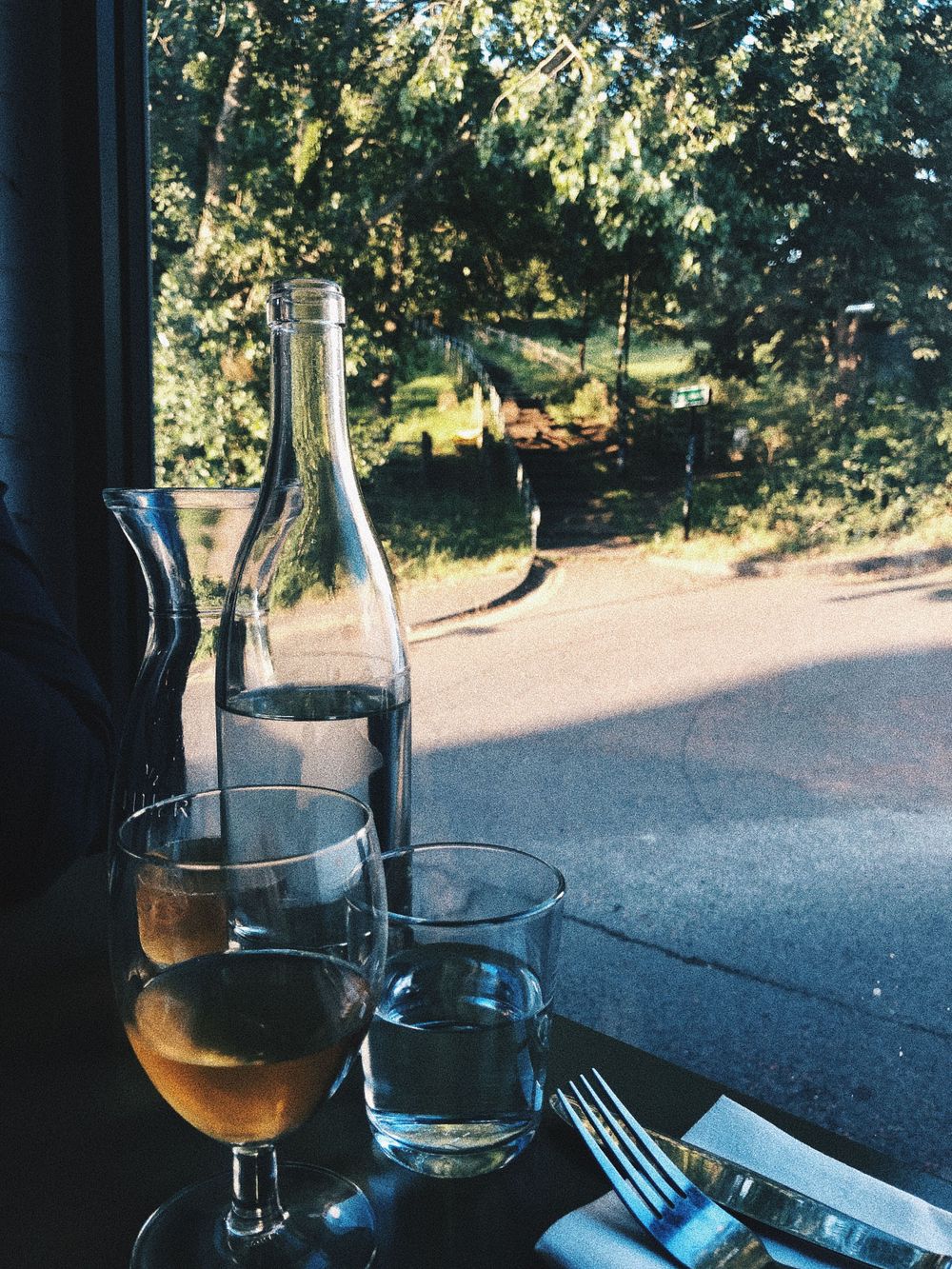 Wine bottle and glasses on a table with sunset view through window.