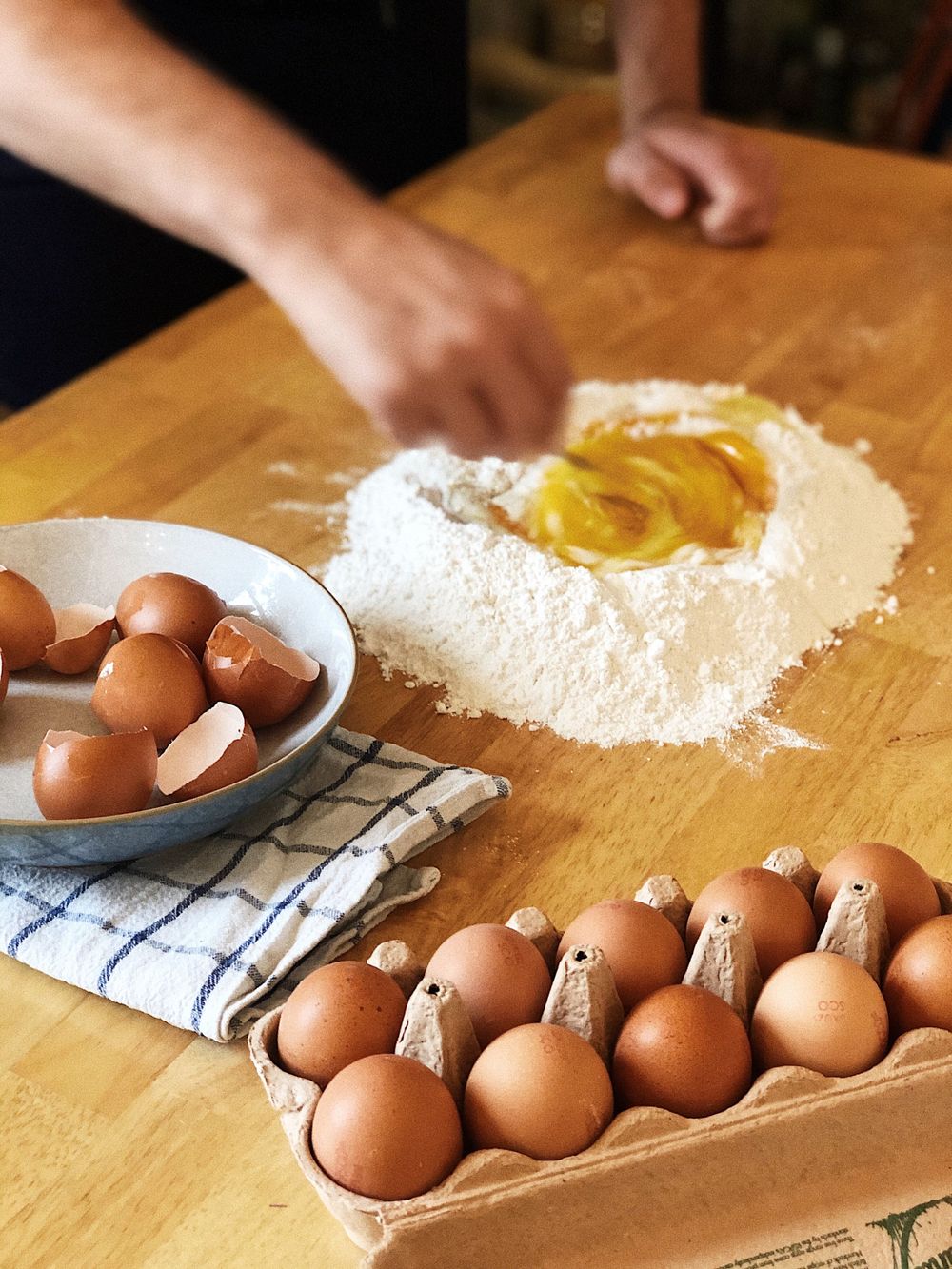 Fresh eggs and flour with well technique for making pasta dough on wooden surface.