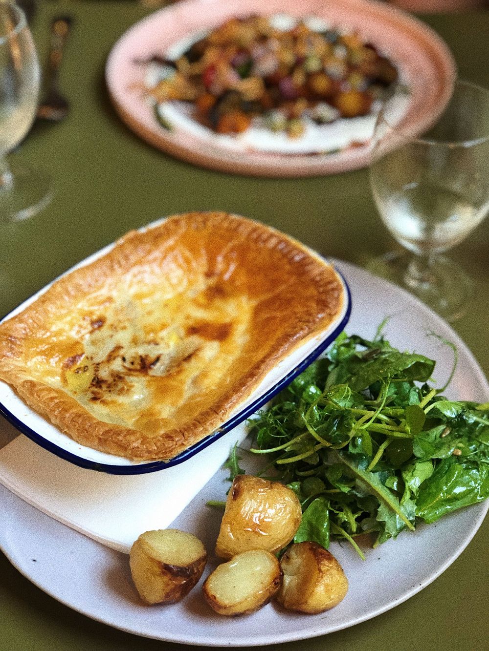 Golden brown pot pie served with roasted potatoes and fresh arugula salad on a white plate.