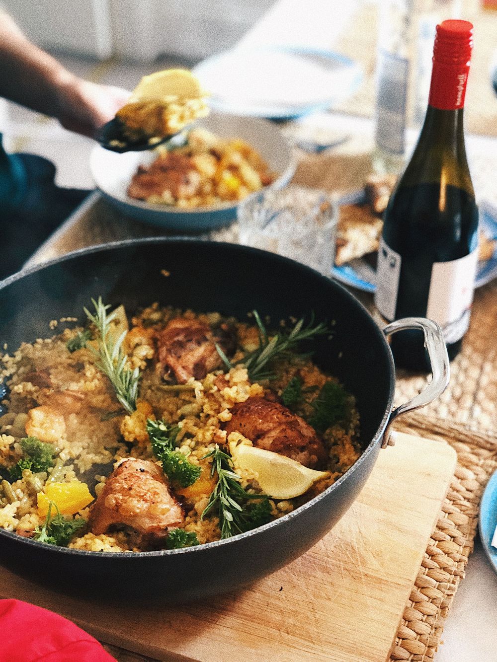 Pan-seared chicken with rosemary and lemon served with rice and a bottle of red wine in a rustic setting.