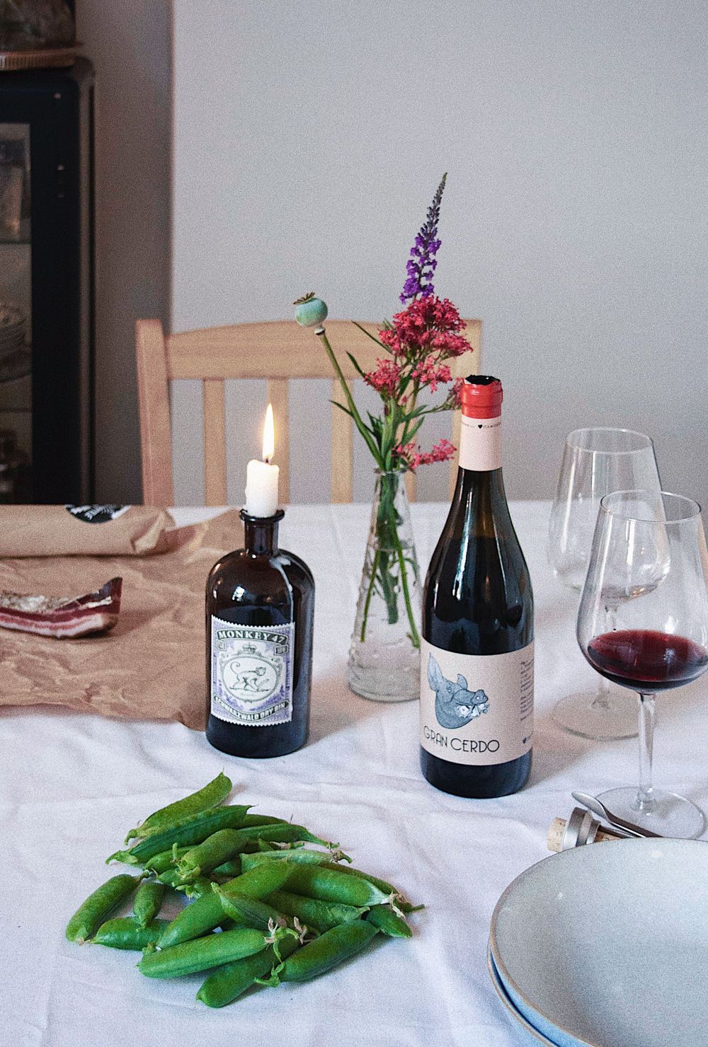 Table setting with wine bottles, snap peas, and purple flowers in a vase with candlelight.