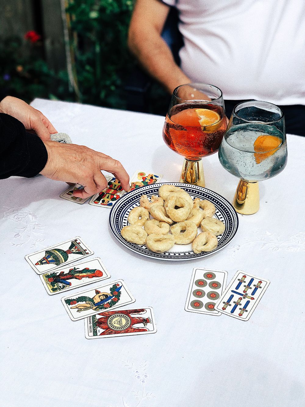 A game table with playing cards and taralli snacks arranged with glasses of cocktails.