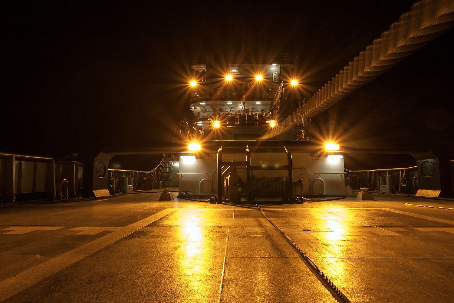 Ship's deck illuminated at night with bright spotlights creating dramatic golden reflections.