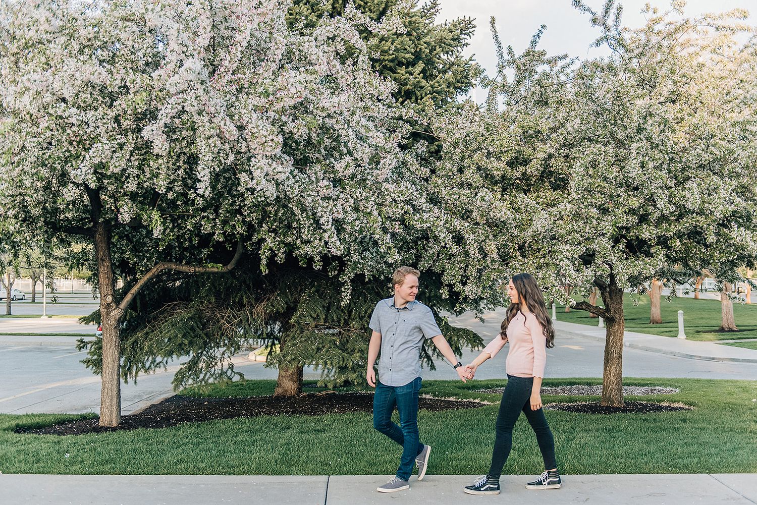 A couple walks together beneath flowering trees on a spring day.