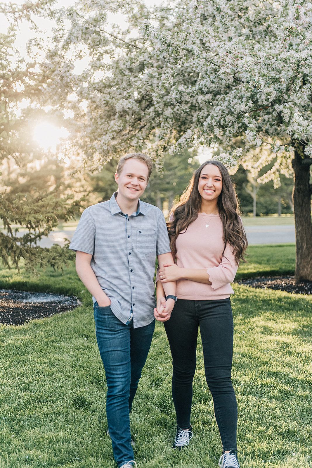 A couple stands together under blooming spring trees at sunset in a park setting.