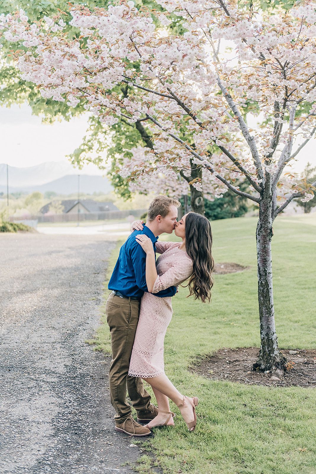 A romantic moment shared under a blooming cherry blossom tree beside a path.