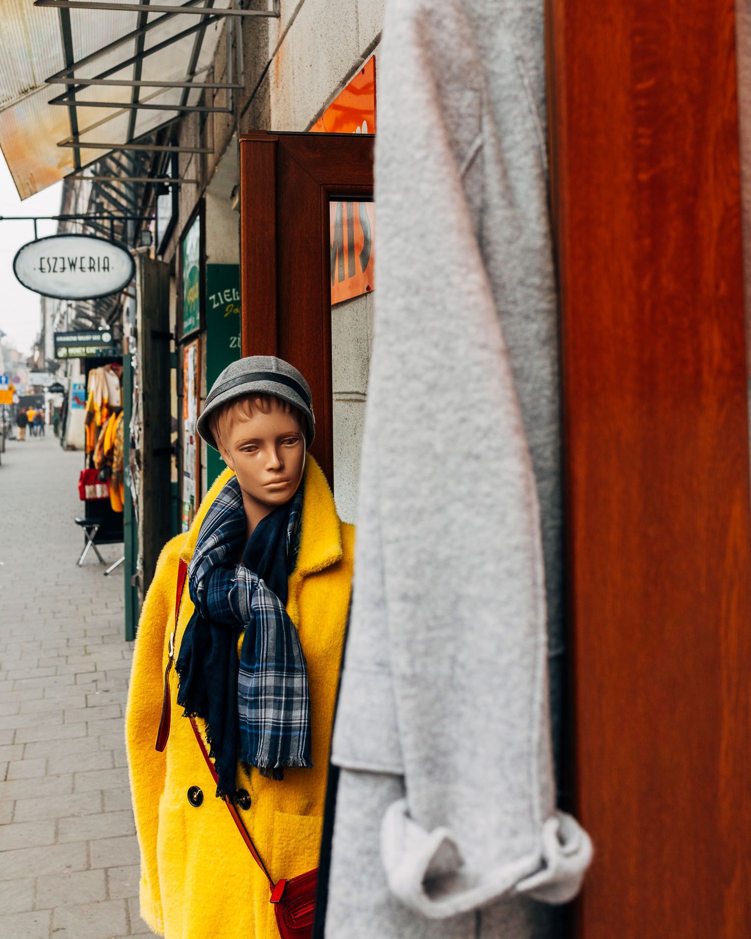 Person wearing bright yellow coat standing on city sidewalk near shop signs.