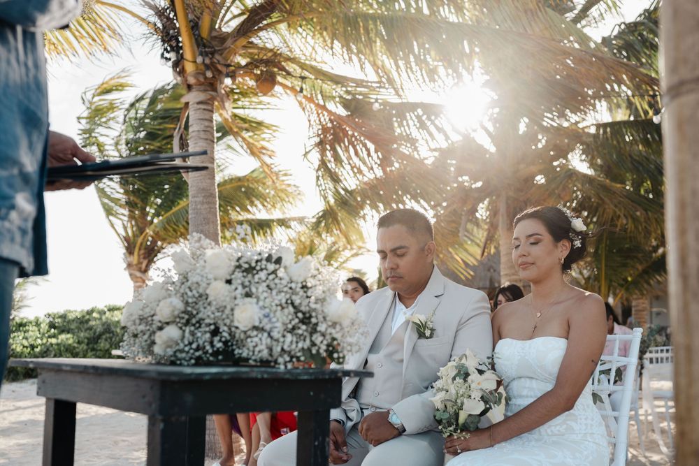 Wedding party celebrates on a tropical beach with palm trees and sunlight creating a dreamy atmosphere.