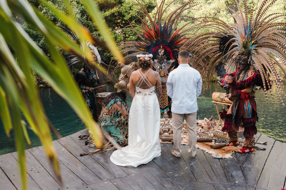 Traditional dancers in colorful feathered headdresses perform at an outdoor wedding celebration, Sandos Caracol Wedding Cenote.
