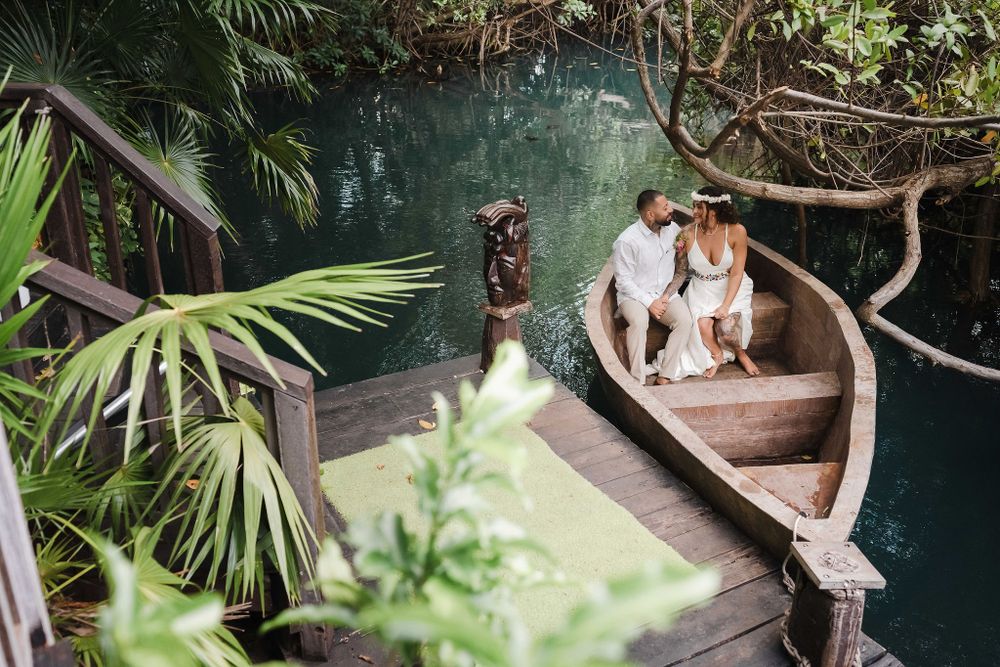 Wooden boardwalk surrounded by lush tropical foliage and palm trees near water, Sandos Caracol Wedding Cenote.