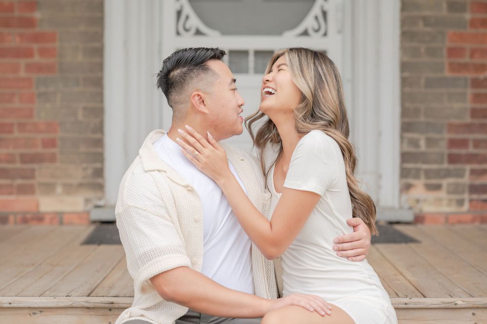 Couple in coordinated white outfits embracing lovingly on outdoor steps of historic building.