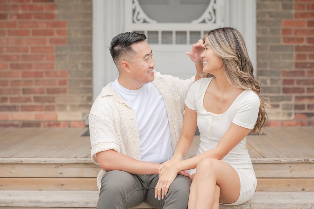 Romantic couple in matching white outfits share tender moment on brick building steps.