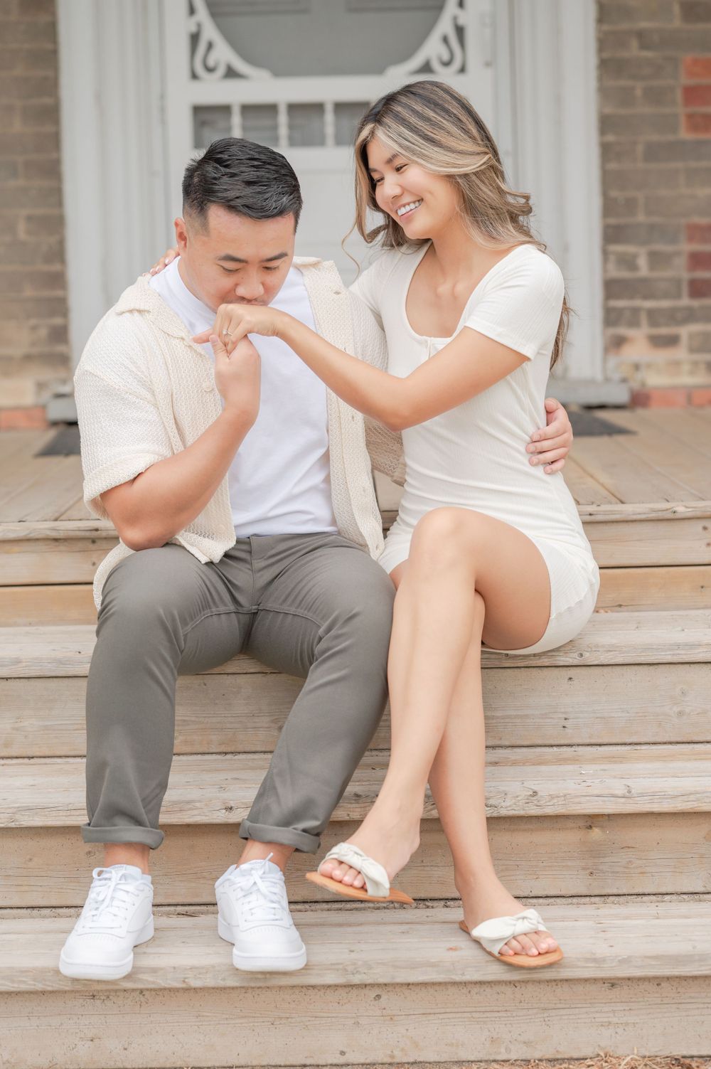 Sweet romantic gesture between couple dressed in white sitting on vintage porch steps.