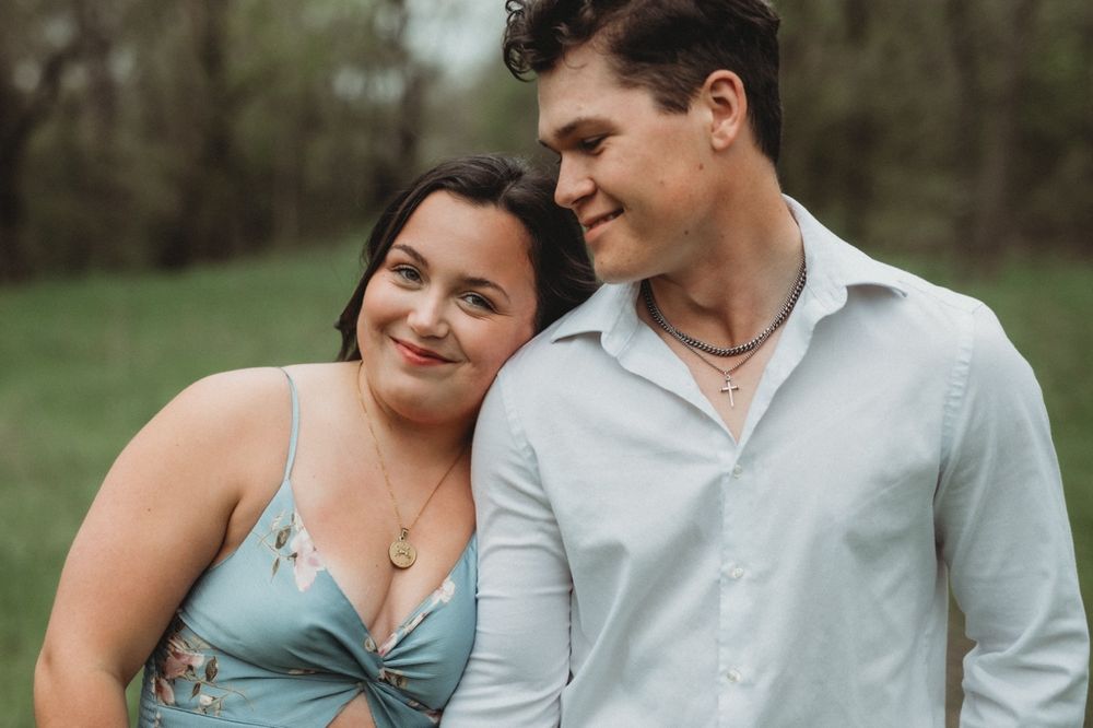 A couple shares an intimate moment outdoors in casual attire against a natural background.