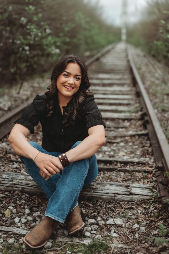 Woman in casual attire sits comfortably on railroad tracks during a photo shoot.