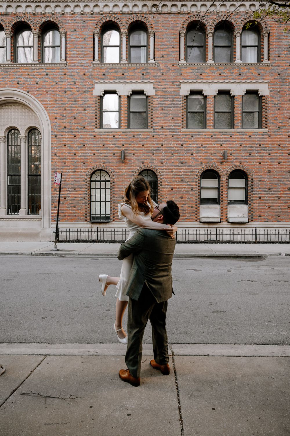 A couple dances intimately in front of a historic brick building with arched windows.