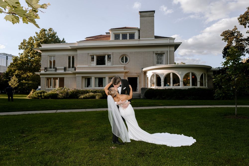 A scenic wedding venue with white Mediterranean-style architecture sits atop a lush green hillside on a sunny day.