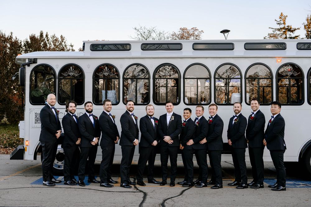 Large white party bus with wedding party members lined up in front of it.