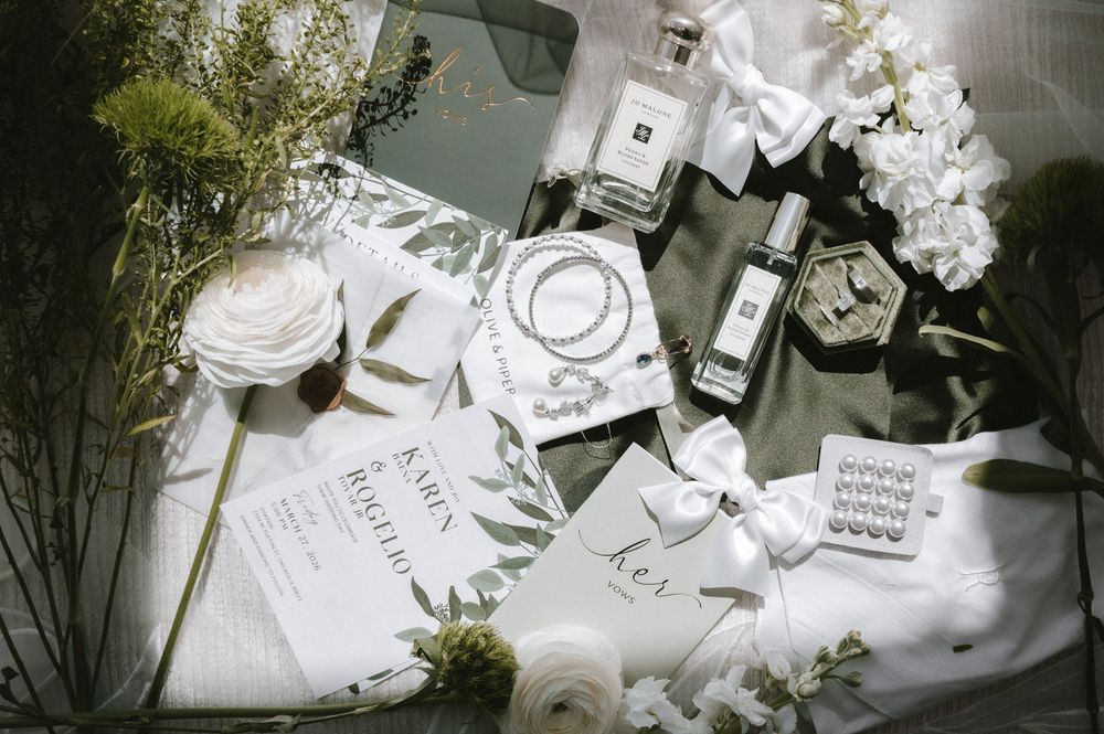 Elegant flat lay of Jo Malone perfume, white roses, pearl jewelry, and gift boxes on a soft green background.