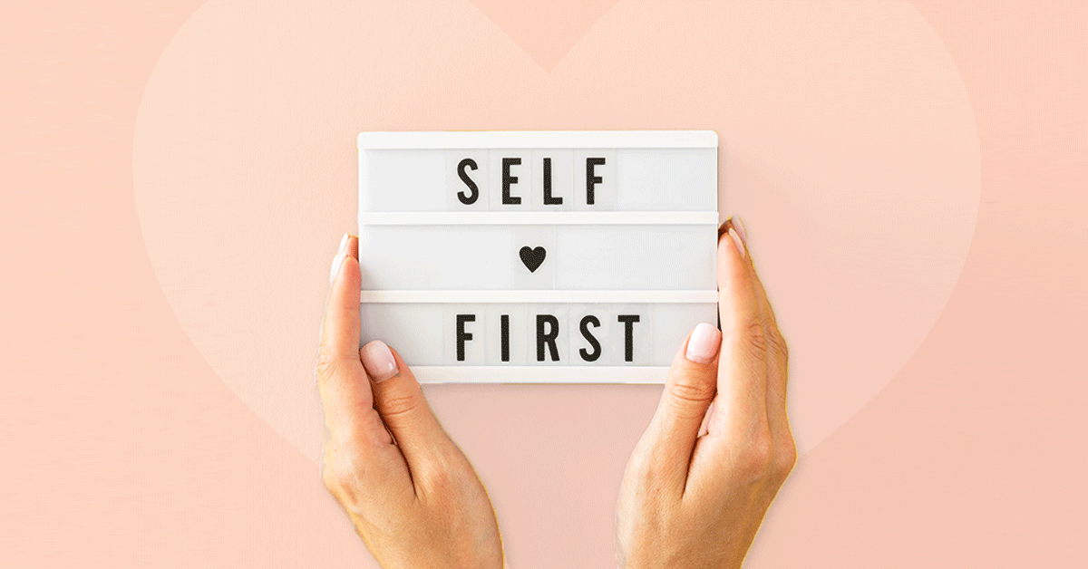 Hands holding lightbox sign with 'SELF FIRST' text on pink background.