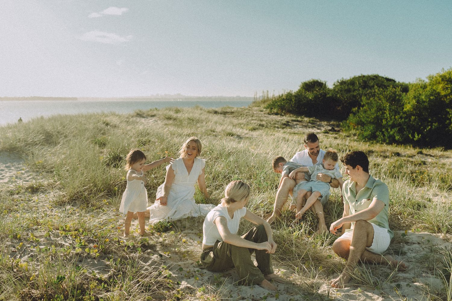 A large family gathered together on the grassy dunes of Kurnell Beach, enjoying a sunny day.