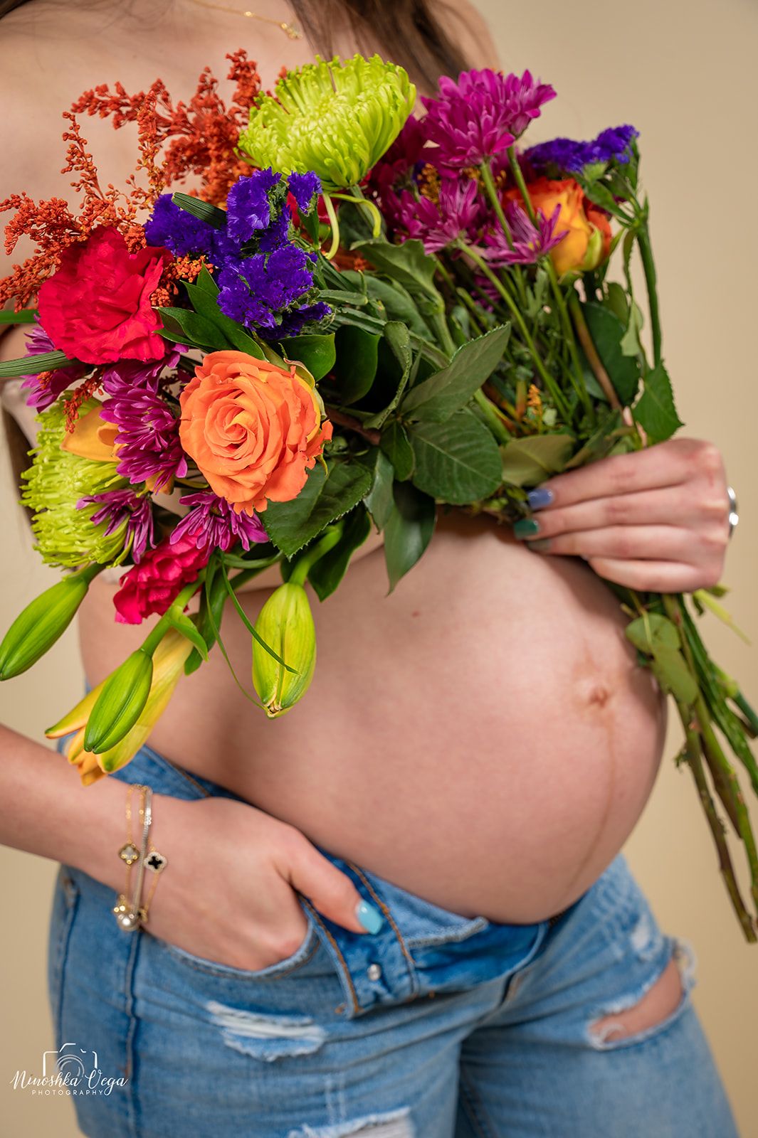 Vibrant floral maternity photos with colorful bouquet against beige background.