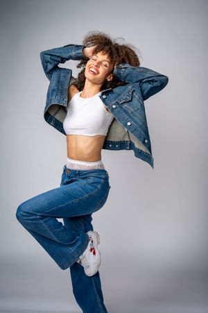 Dynamic fashion shoot with model in denim outfit dancing against gray backdrop.