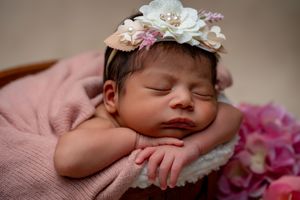 Newborn photography with delicate white and pink floral headpiece decorations.