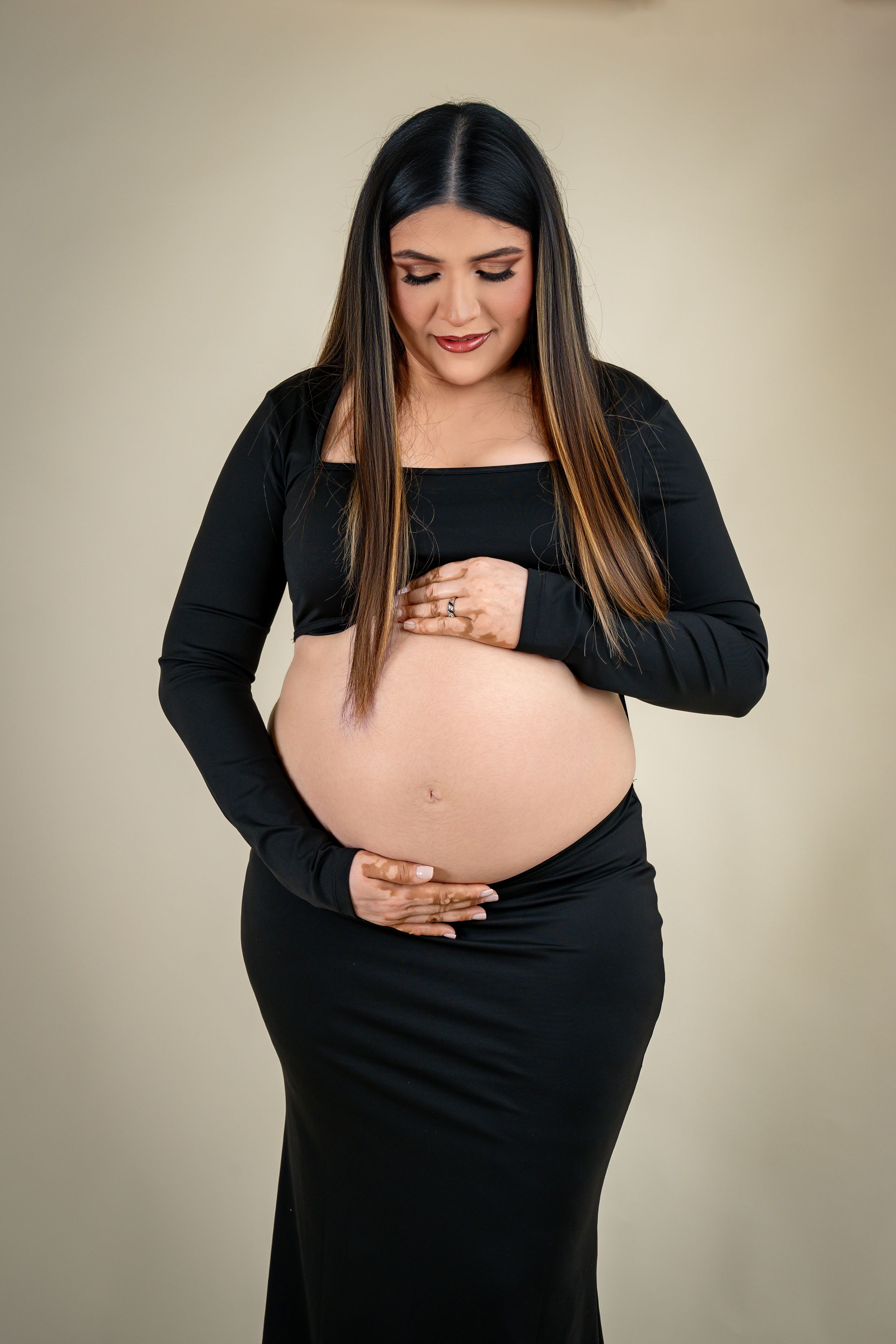 Maternity photo series showing a woman in black dress cradling her pregnant belly against a neutral background.