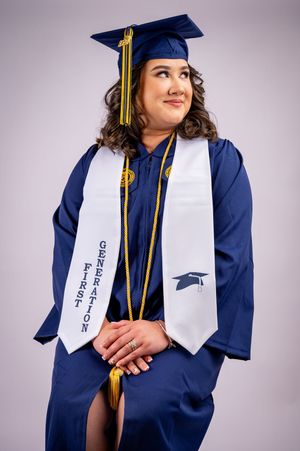 Graduate in navy blue cap and gown with white sash posing for portraits.