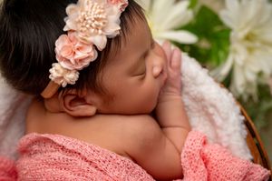 Newborn baby sleeping peacefully in pink lace wrap with matching floral headband in natural light setting.