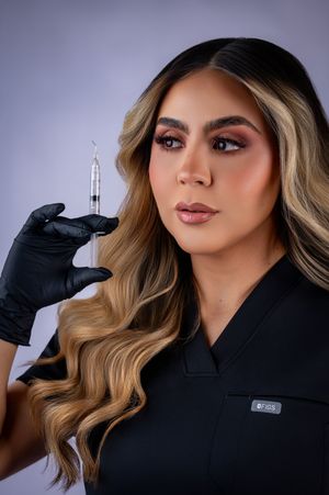 Medical professional in black scrubs and gloves holds syringe against purple backdrop with styled blonde wavy hair.