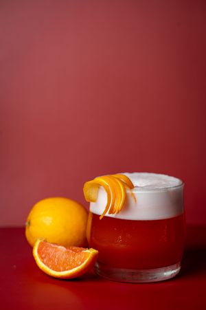 Fresh orange slices arranged beside a white glass container against a deep red background in minimalist composition.