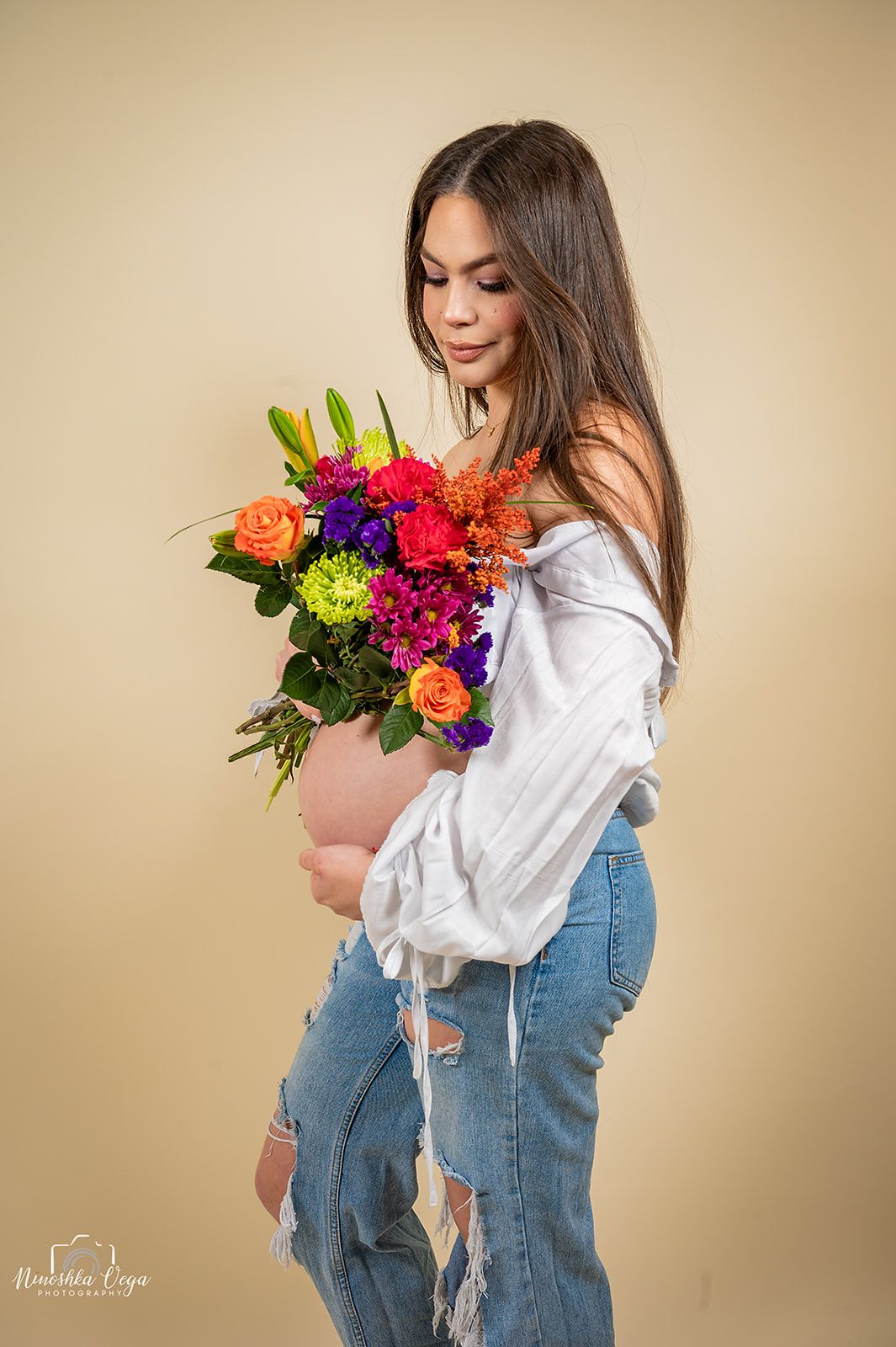 A person in denim overalls and white blouse holds a vibrant bouquet of colorful flowers against a beige backdrop.